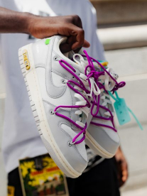 A pair of grey, white and purple Nike sneakers being held in a mans hand.